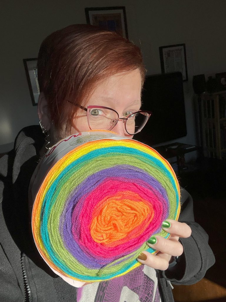 Me holding a large cake of rainbow colored yarn
